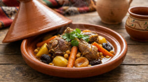 Tajine d'agneau fraîchement préparé, débordant de légumes colorés, fruits secs et pois chiches, sur une table en bois rustique.